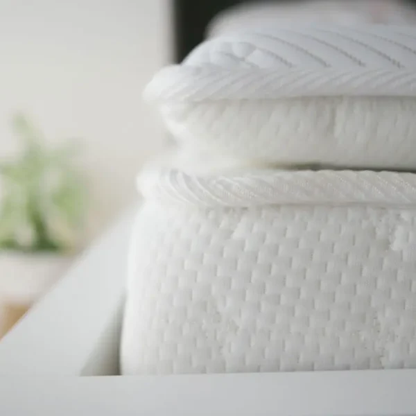 Close-up of stacked white mattresses on bed frame.