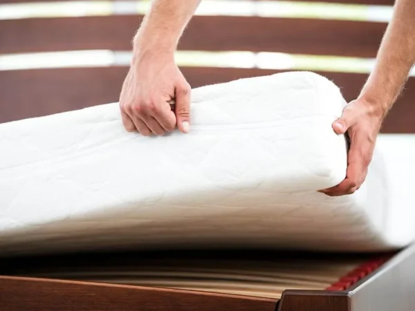 Person lifting a mattress on wooden bed frame.