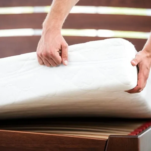 Person lifting a mattress on wooden bed frame.