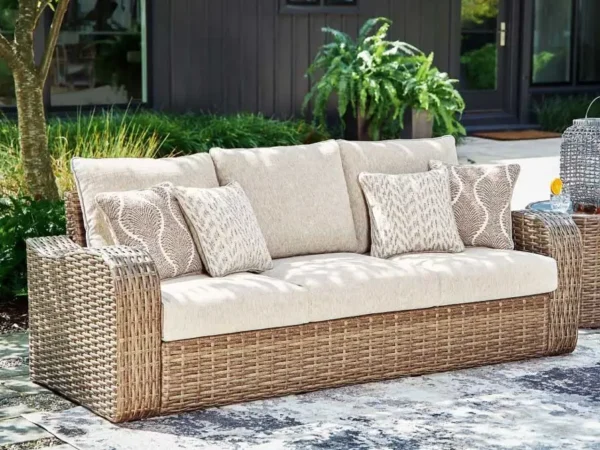 Outdoor wicker sofa with beige cushions and pillows.