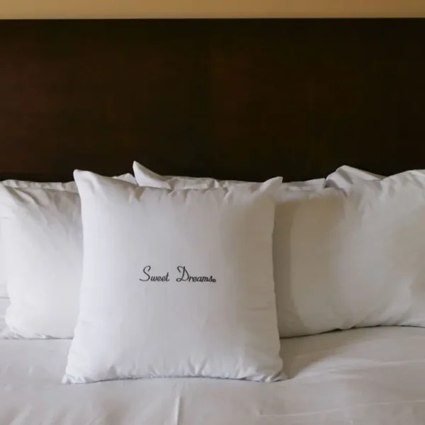 White pillows on bed, one says 'Sweet Dreams'.