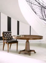 Round wooden dining table and tufted leather chair by staircase.