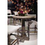 Ornate wooden pedestal table with vibrant flowers and white stools.