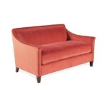 Coral velvet loveseat with nailhead trim and dark wood legs.