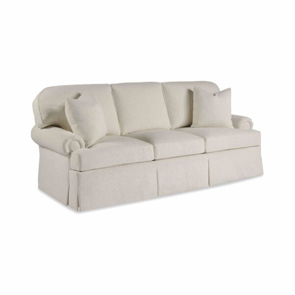 Cream-colored three-seater skirted sofa with rolled arms and pillows.
