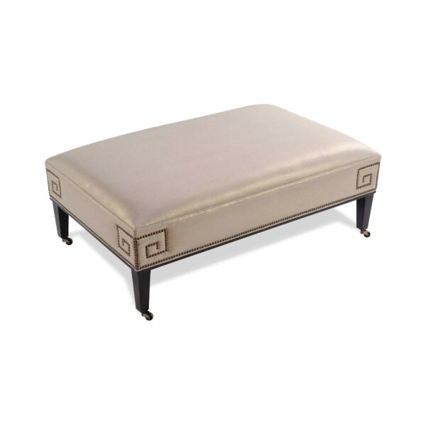 Champagne upholstered ottoman with Greek key nailhead trim and casters.